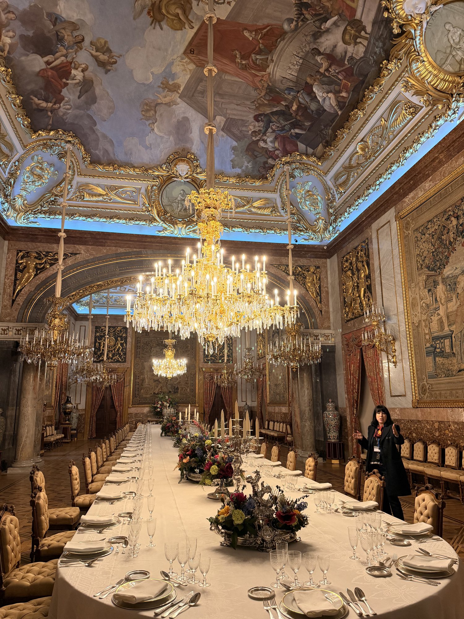 The Gala Dining Room inside the Royal Palace of Madrid with a long banquet table, chandeliers, and a painted ceiling